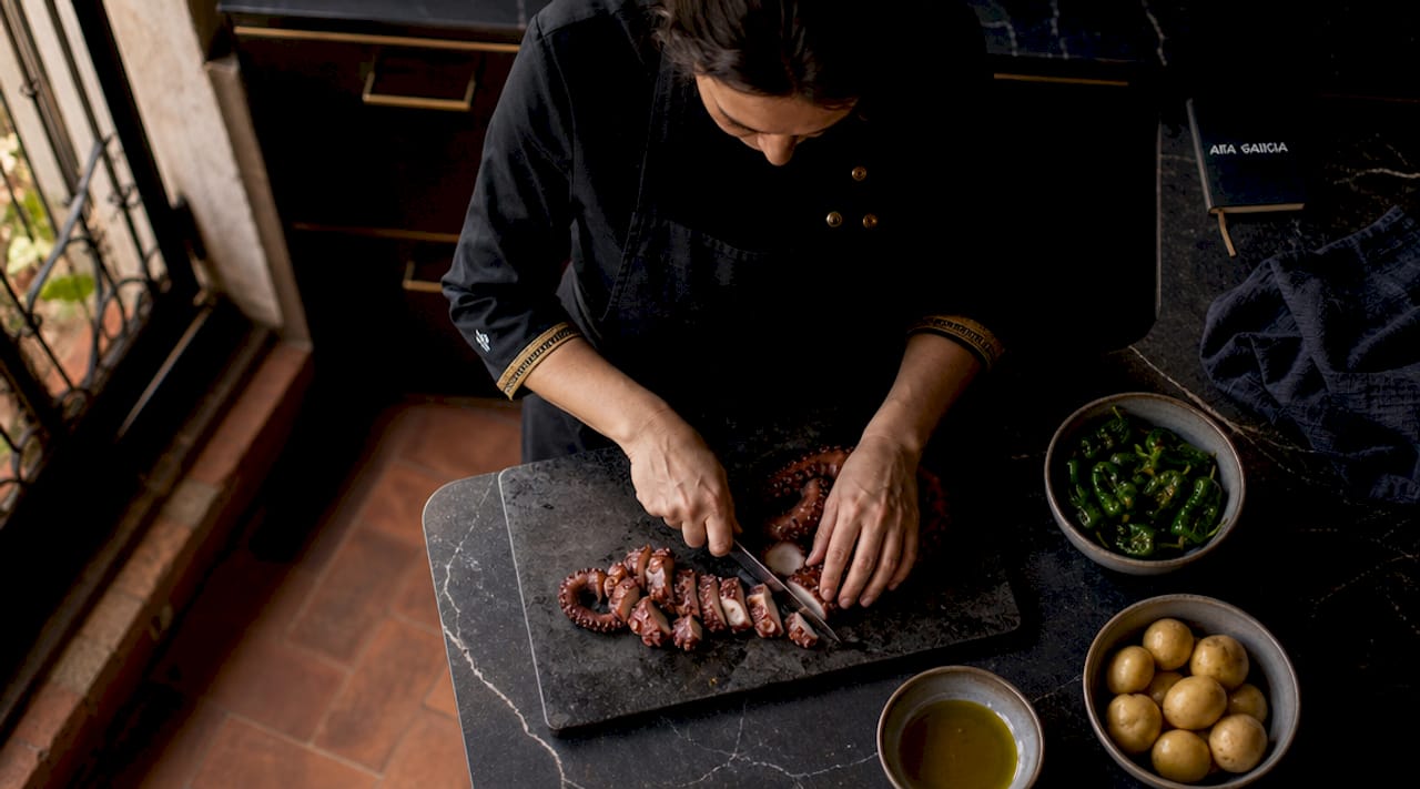 Un chef elabora un plato típico gallego en una cocina de estilo rústico.