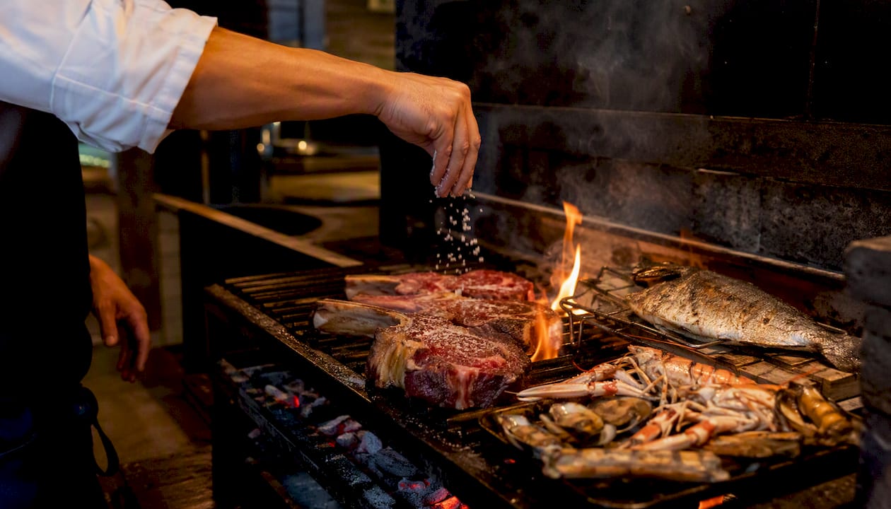 Parrilla de carbón llena de carnes y mariscos asándose, lista para disfrutar de una buena comida al aire libre.