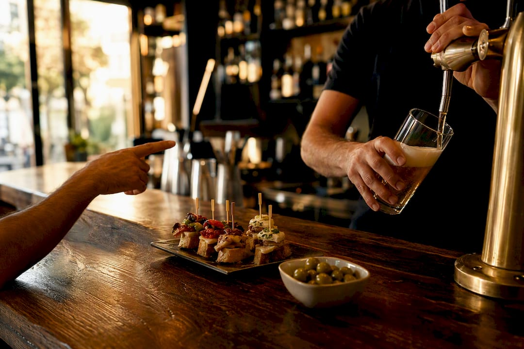 Mano pidiendo una caña en la barra de un bar español